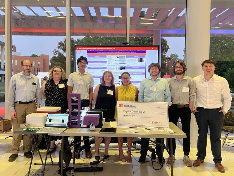 Seven-person Clemson senior-design team standing behind the Drosophila prototype and showcase poster